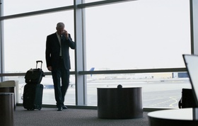 Geschäftsmann mit Gepäck telefoniert am Flughafen