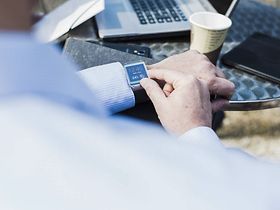 Geschäftsmann schaut in Café auf Smart Watch