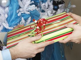 Hände übergeben Geschenk vor Weihnachtsbaum