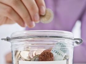 Hand gibt Münze in Einmachglas als Spardose