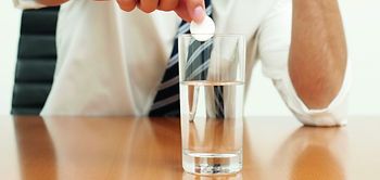 Hand löst Tablette in Glas Wasser auf