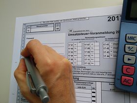 Hand schreibt in USt-Voranmeldung/Umsatzsteuer-Voranmeldung