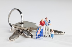 A young family of miniature figurines standing next to house keys on a key ring