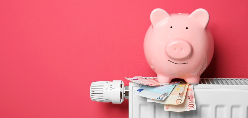 Savings concept. Piggy bank and money on heating radiator with temperature regulator on pink backgro