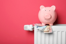 Savings concept. Piggy bank and money on heating radiator with temperature regulator on pink backgro