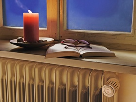 Heizkoerper unter altem, undichtem Fenster, Kerze, Buch