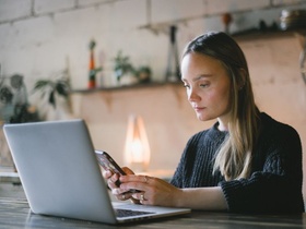 Jobsuche: Frau schaut vor Laptop auf ihr Smartphone