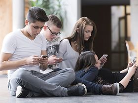 Jugendliche auf dem Boden mit Smartphones von der Seite