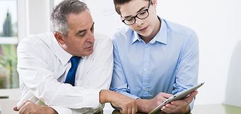 Jugendlicher und älterer Mann schauen auf ein Tablet