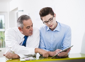 Jugendlicher und älterer Mann schauen auf ein Tablet