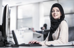 junge Frau mit Kopftuch arbeitet an Desktop