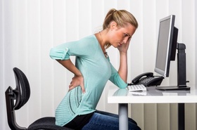 Junge Frau mit Rückenproblemen am Arbeitsplatz
