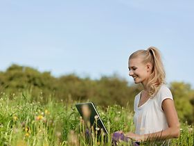 Junge Frau sitzt in Wiese mit Laptop
