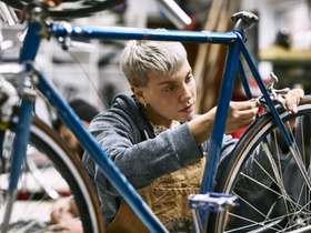Young female mechanic repairing bicycle brake at workshop. Confident employee is working at repair s