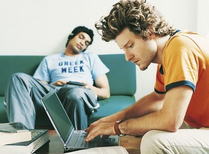 Junger Mann am Computer, junger Mann schläft im Hintergrund