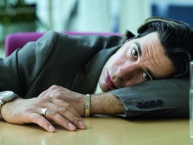 Junger Mann liegt auf Arm gelehnt auf Schreibtisch