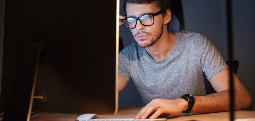 Junger Mann mit Brille sitzt vor Computer und schaut angestrengt auf Bildschirm