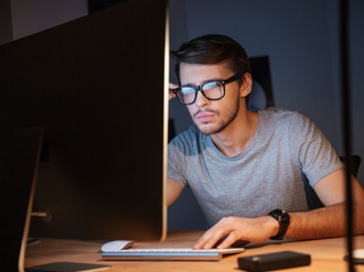 Junger Mann mit Brille sitzt vor Computer und schaut angestrengt auf Bildschirm