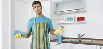 Junger Mann mit Schürze putzt in der Küche