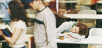 Junger Mann schläft in Hörsaal, junge Leute gehen hin und her