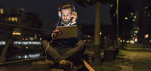 junger Mann sitzt auf Parkbank und hört Musik im Dunkeln