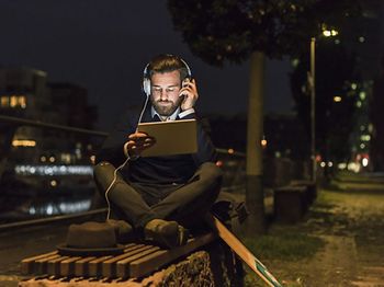 junger Mann sitzt auf Parkbank und hört Musik im Dunkeln