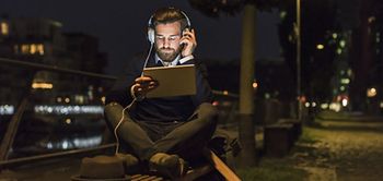 junger Mann sitzt auf Parkbank und hört Musik im Dunkeln