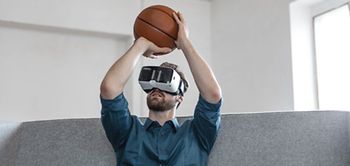 junger Mann spielt auf Sofa Basketball mit VR-Brille