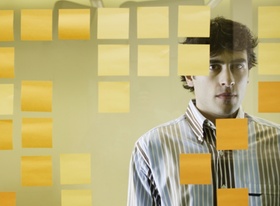 Junger Mann steht nachdenklich vor Glaswand mit Post its