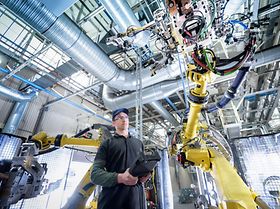 junger Mitarbeiter in Fabrik arbeitet mit Roboter