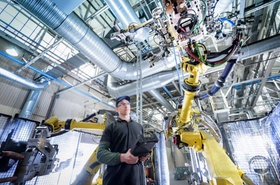 junger Mitarbeiter in Fabrik arbeitet mit Roboter