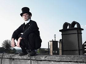 Kaminkehrer hockt neben Kamin auf Dach