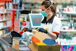 Woman cashier wearing protective face mask and gloves to prevent viruses, scanning disinfection prod