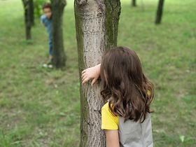 Kinder spielen hinter Baeumen verstecken