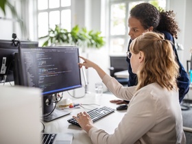 Businesswoman discussing computer program with female colleague at desk in creative office