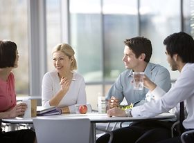Kollegen sitzen essend an Tisch und unterhalten sich