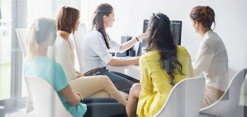 Kollegin zeigt Mitarbeitern etwas am Bildschirm