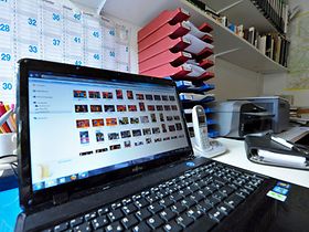 Laptop groß im Vordergrund auf Schreibtisch - dahinter Ablagekörb