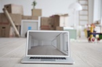 Laptop mit Bild von Wohnung steht vor Umzugskartons