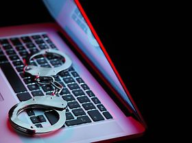 Laptop vor schwarzem Hintergrund mit Handschellen