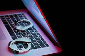 Laptop vor schwarzem Hintergrund mit Handschellen