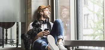Laughing casual young man sitting at the window with dog