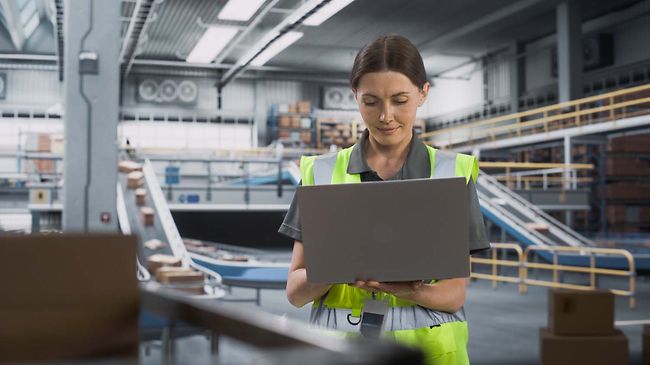 Logistik_Frau mit Laptop vor Paketband