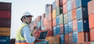 Logistikmitarbeiter mit Laptop mit Frachtcontainern