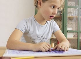 Maedchen sitzt am Tisch beim Malen