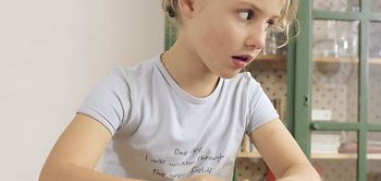 Maedchen sitzt am Tisch beim Malen