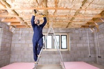 Man in coveralls and protective mask installing ceiling insulation