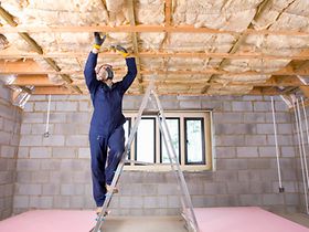 Man in coveralls and protective mask installing ceiling insulatio