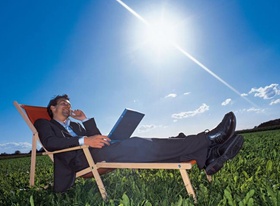 Manager liegt mit Notebook und Handy im Liegestuhl auf Wiese