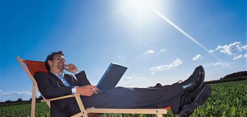 Manager liegt mit Notebook und Handy im Liegestuhl auf Wiese